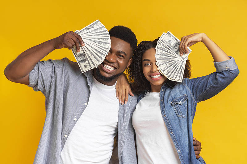Lucky black man and woman holding lots of dollar cash, covering faces with money and cheerfully smiling