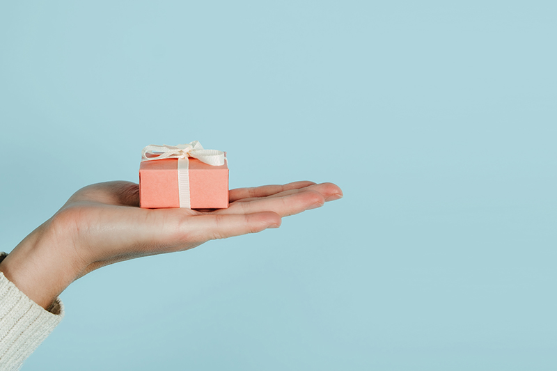Volunteer concept with female hands and pink gift box on blue background.